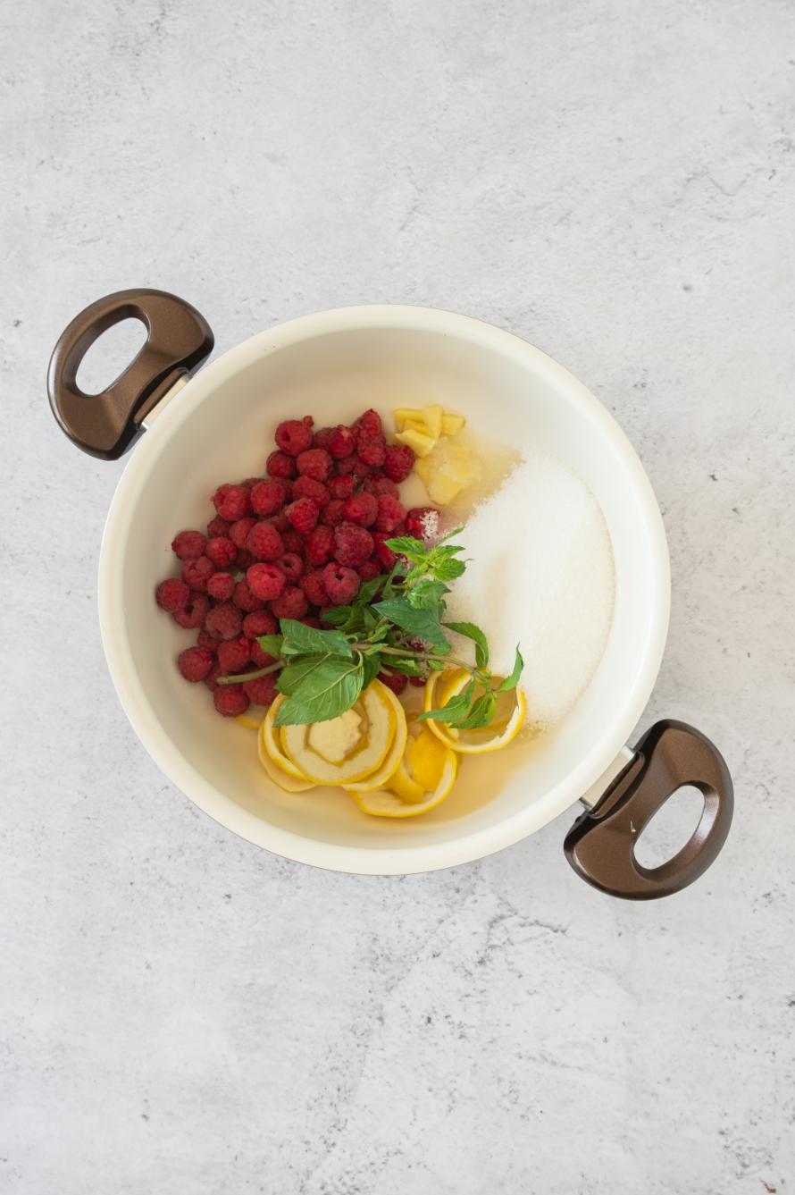 Overhead shot of lemons, raspberries, sugar and mint added to a large saucepan