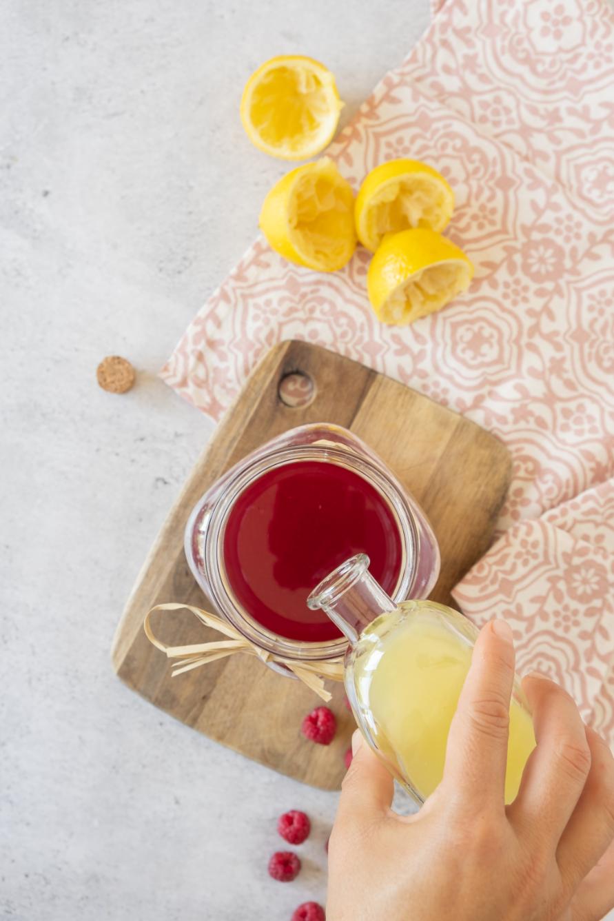 A small vial of lemon juice being added to a raspberry simple syrup