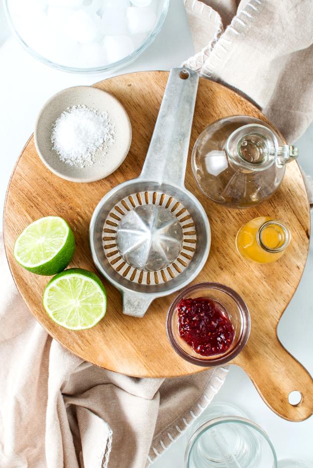 Overhead shot of ingredients including limes, mashed raspberries, apple cider vinegar, soda water and ice