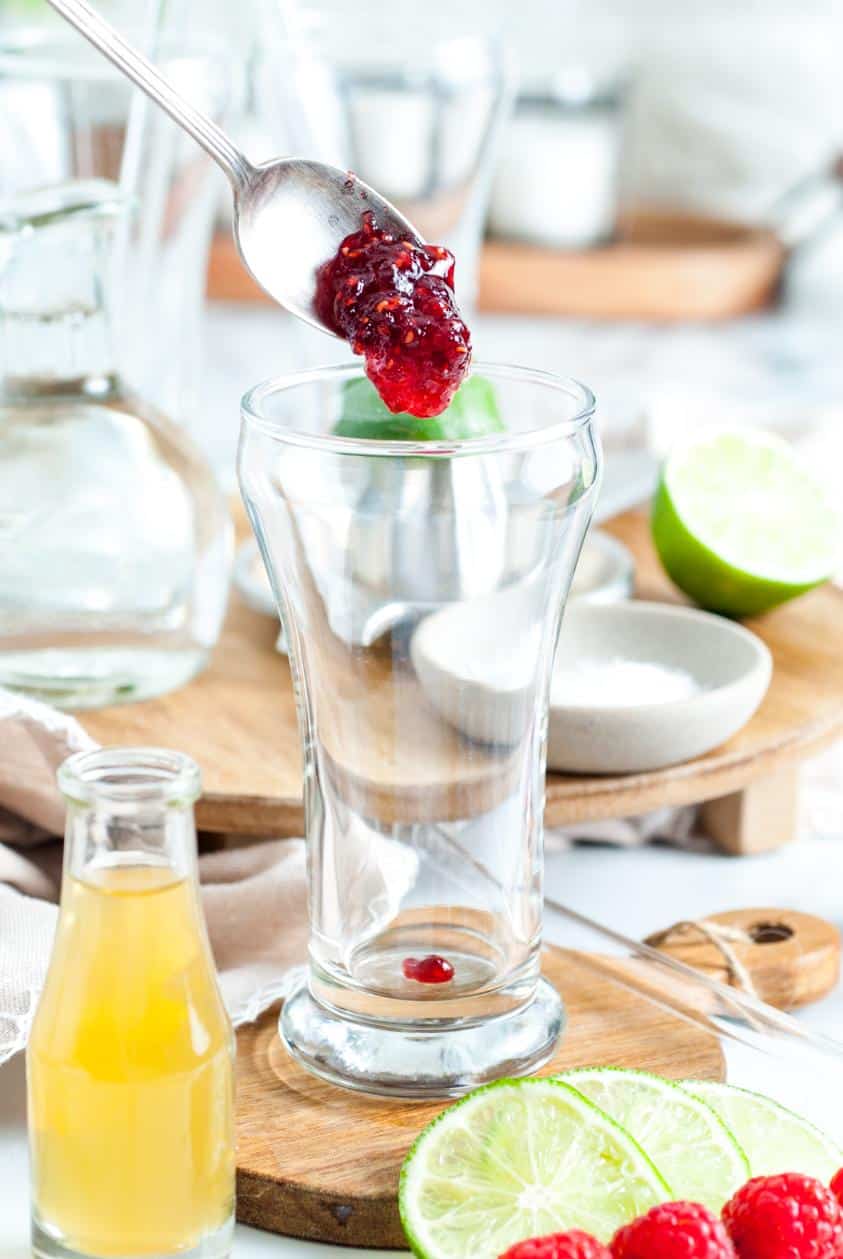 A spoon adding some mashed raspberries to a tall glass