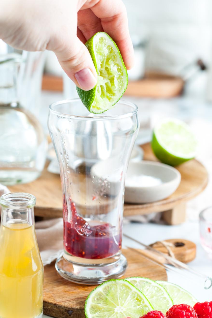 A lime being squeezed into a glass contained mashed raspberries