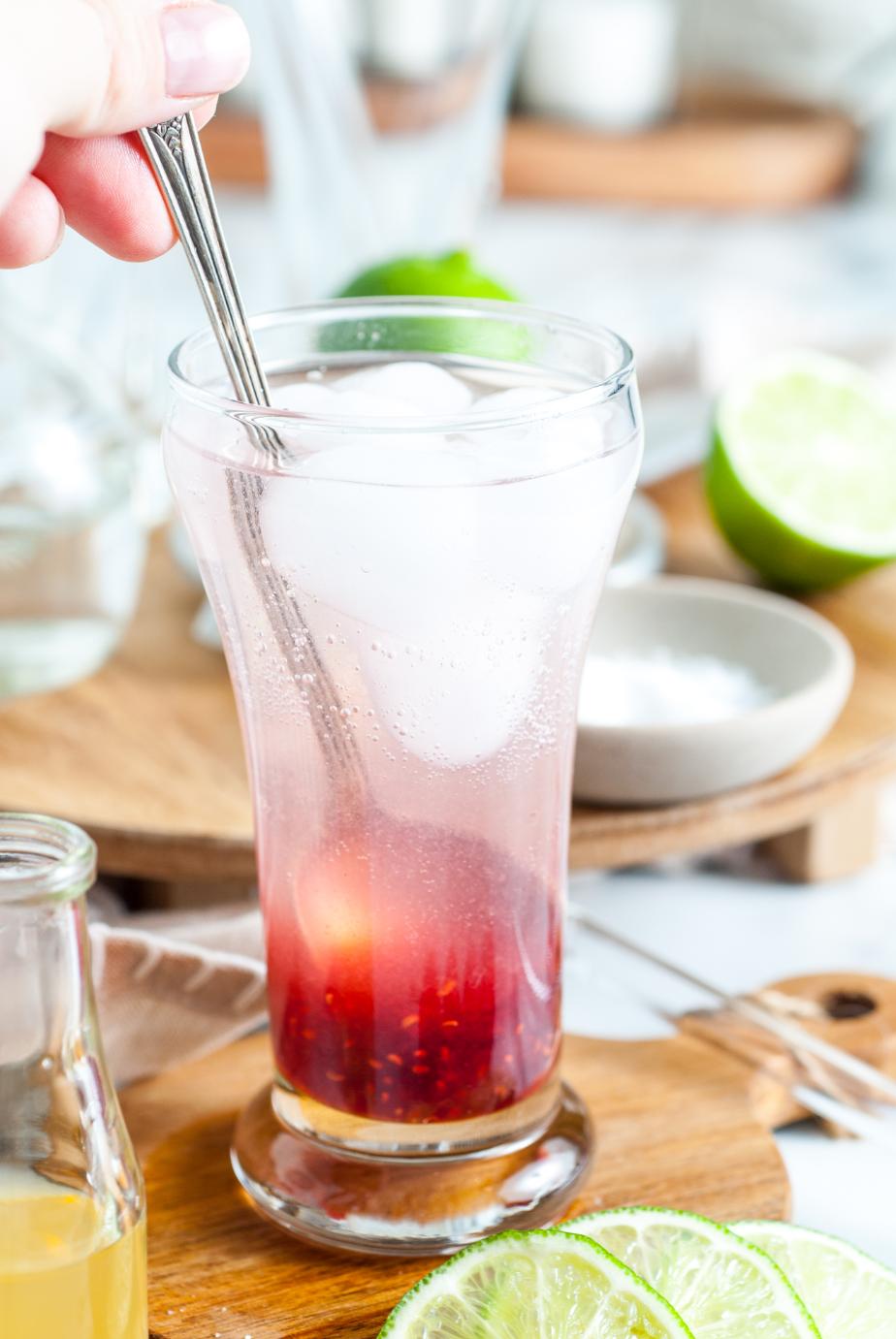 A metal spoon stirring together the ingredients of a mocktail served in a tall glass