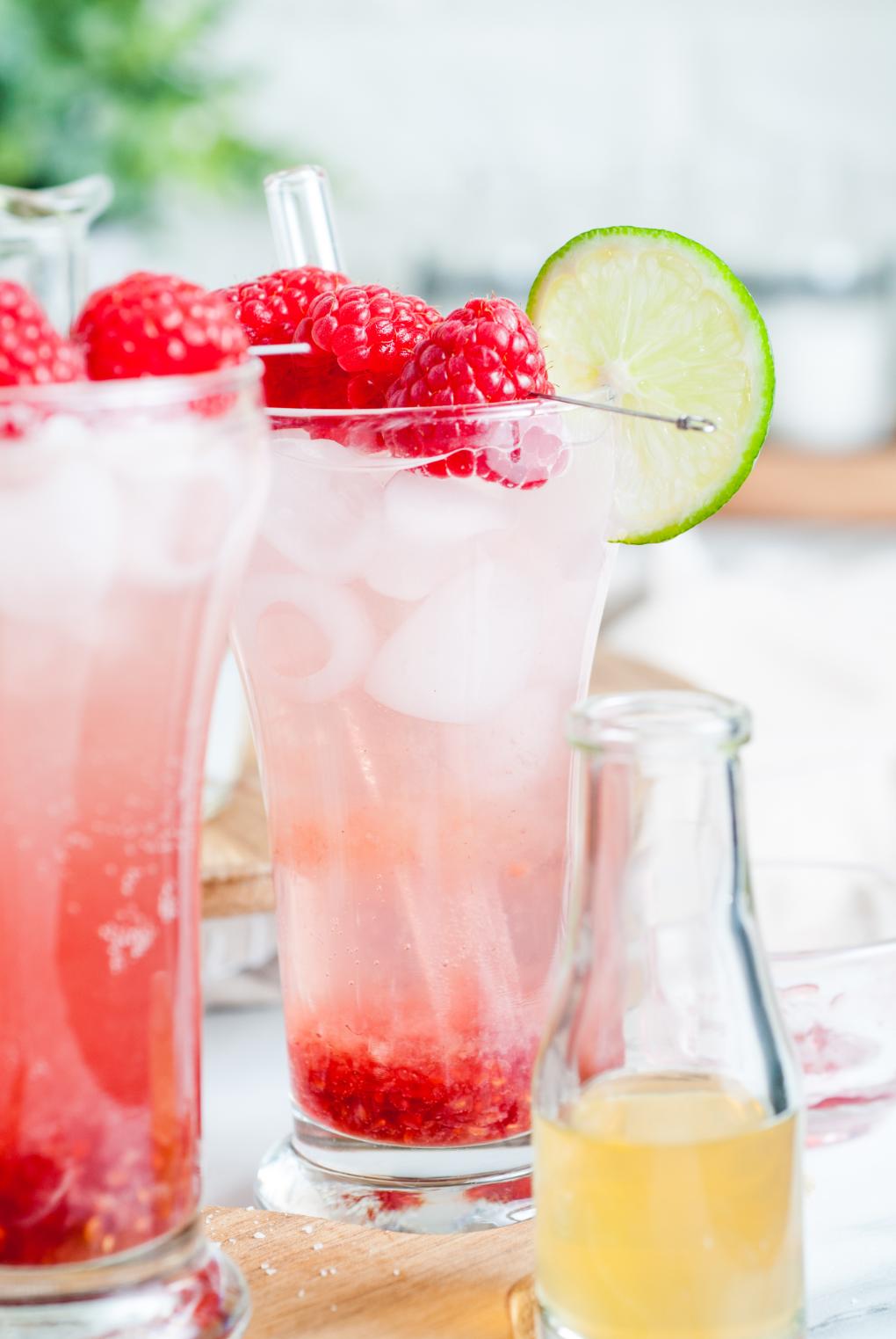 2 raspberry mocktails served in tall glasses with a bottle of apple cider vinegar in front