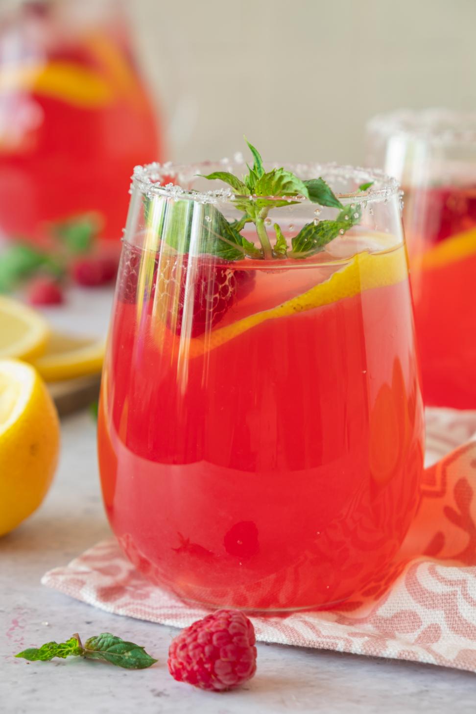 Homemade raspberry lemonade added to a glass with ice, lemon slices and fresh mint