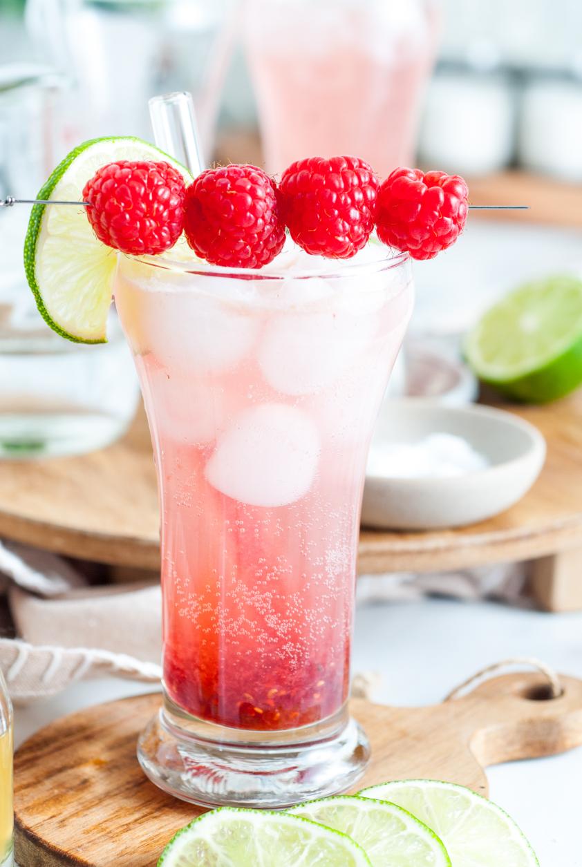 A sparkling red and white drink in a tall glass topped with raspberries