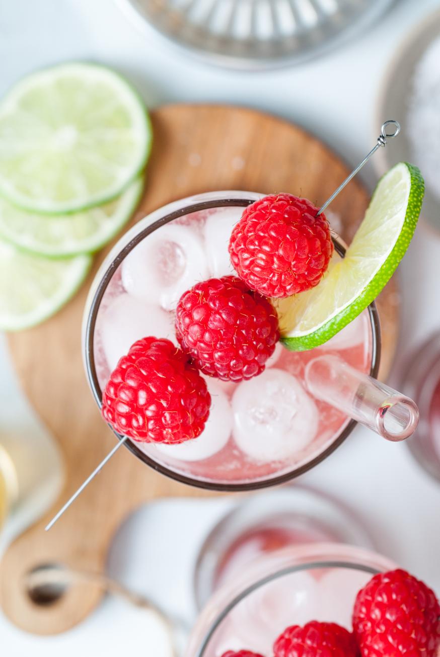 Overhead shot of a sparkling drink with raspberries and lime on top