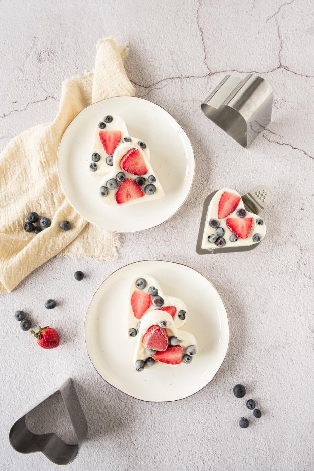 Heart shaped frozen berry yogurts served on white plates with fresh berries in the background