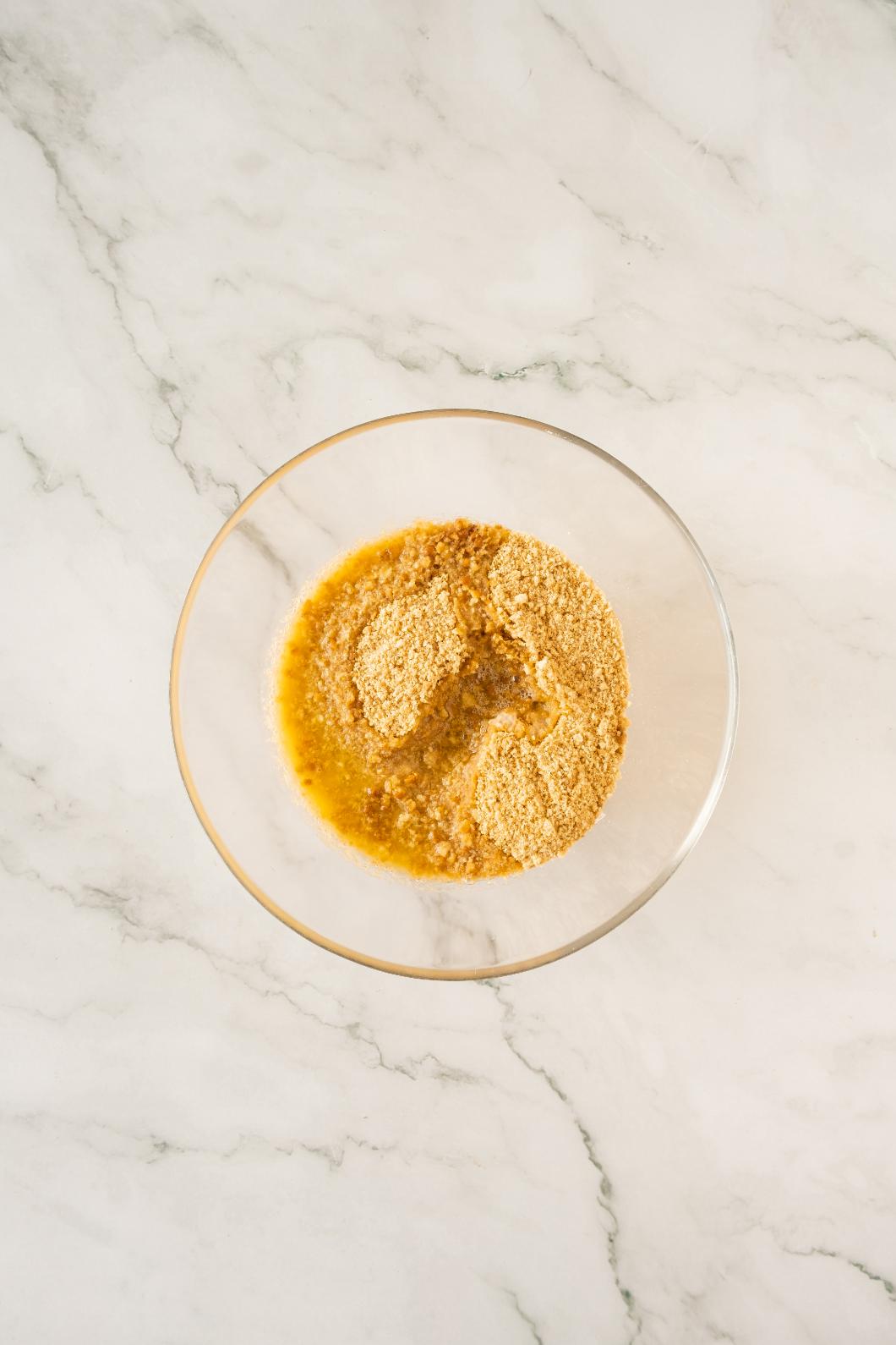 Smashed biscuits combined with melted butter in a glass bowl