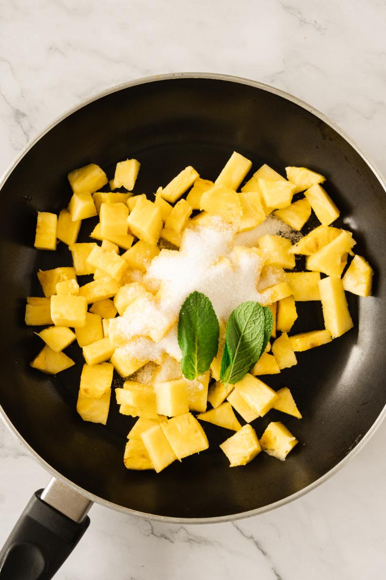 Chunks of pineapple, sugar, and lime in a black saucepan