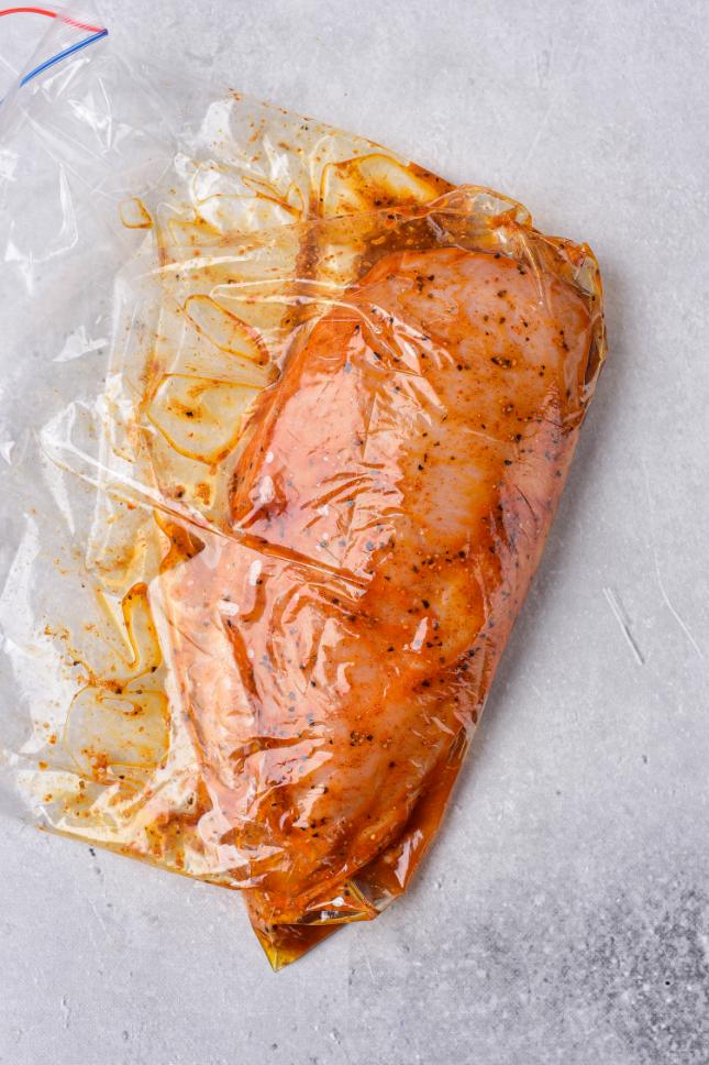 Chicken marinating in herbs and spices and olive oil inside a ziploc bag