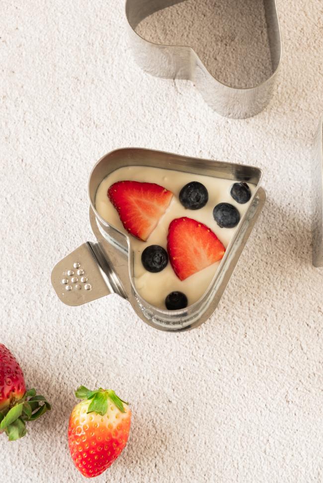 A yogurt mixture poured into a heart shaped mold and topped with fresh slices of strawberry and blueberries