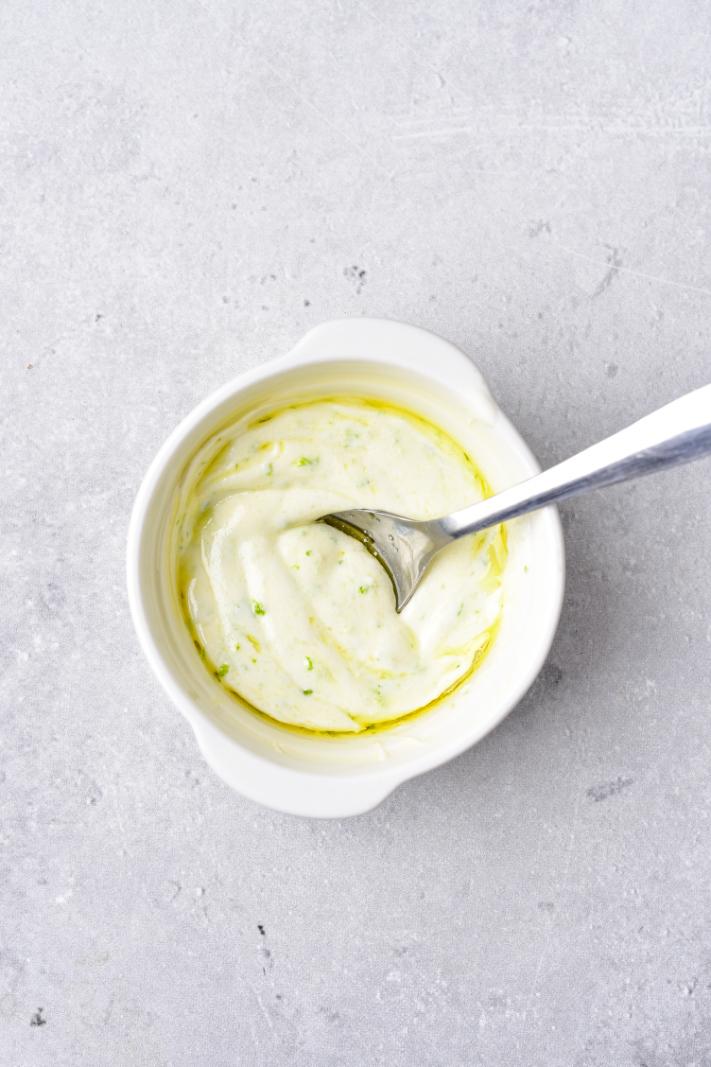 A yogurt salad dressing being mixed with a spoon in a small white bowl