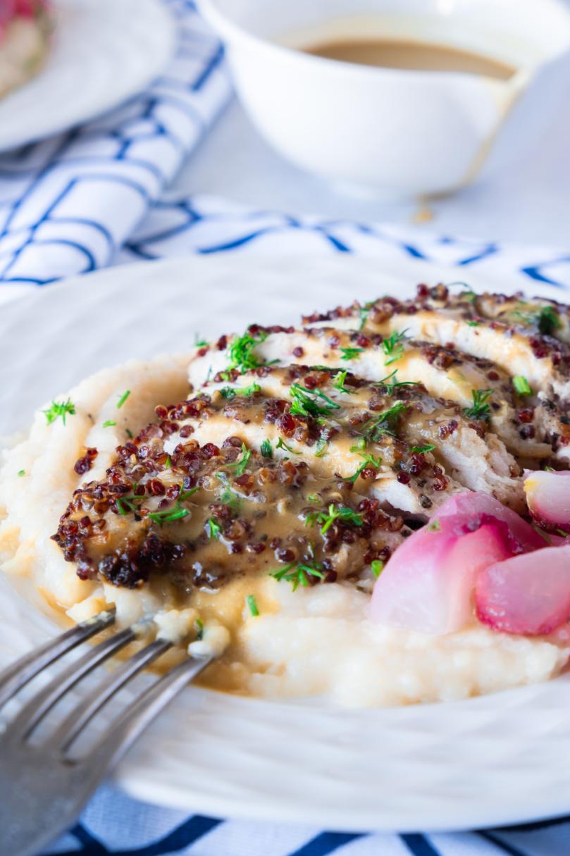 Photo of cooked chicken on top of a bed of mash and topped with fresh herbs