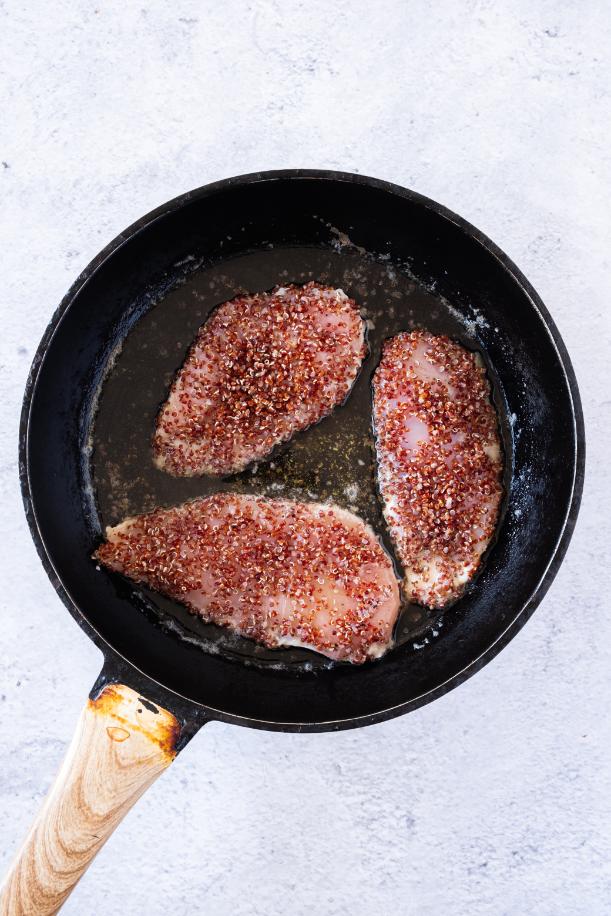 Photo of 3 chicken breasts coated in red quinoa being cooked in a frying pan