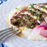 Photo of fried quinoa chicken on a bed of mash with a mustard sauce poured over the top and sprinkled with fresh herbs