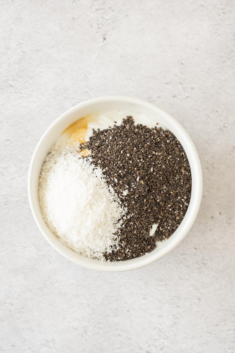 A bowl containing a mixture of black chia seeds, white coconut flakes, honey, and yogurt.