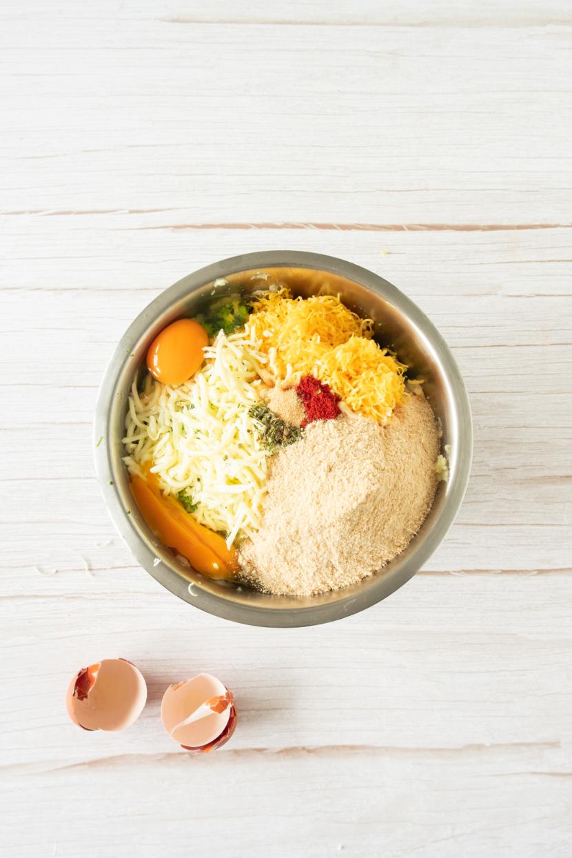 Cooked potato, broccoli and cheese added to a stainless steel bowl with some eggshells on the side