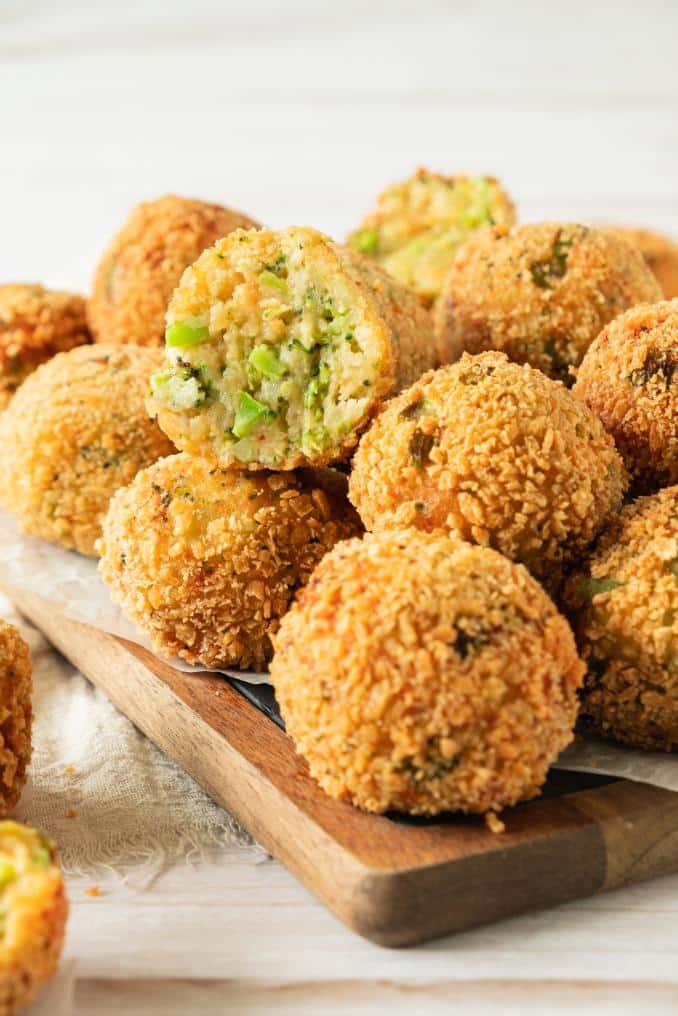 A stack of crispy cheese broccoli bites on a wooden board with some shaved parmesan in the background