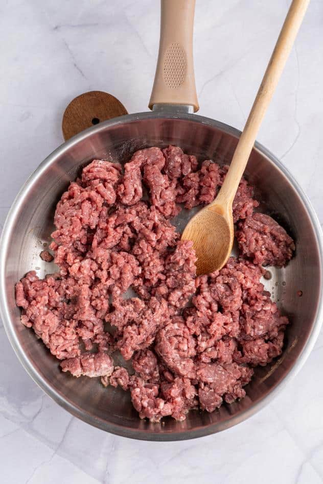 A wooden spoon mashing ground beef as it cooks in a saucepan