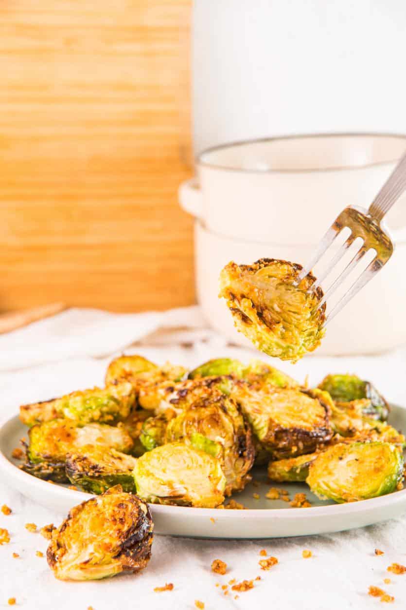 Air fryer brussels sprouts stacked on a white plate. A fork has pierced one and it is being lifted into the air.