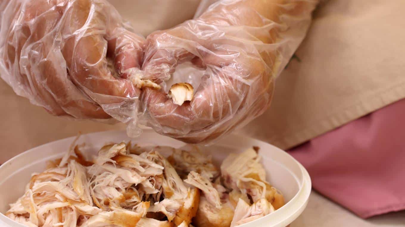 Person wearing gloves while removing chicken from the bone in a rotisserie chicken