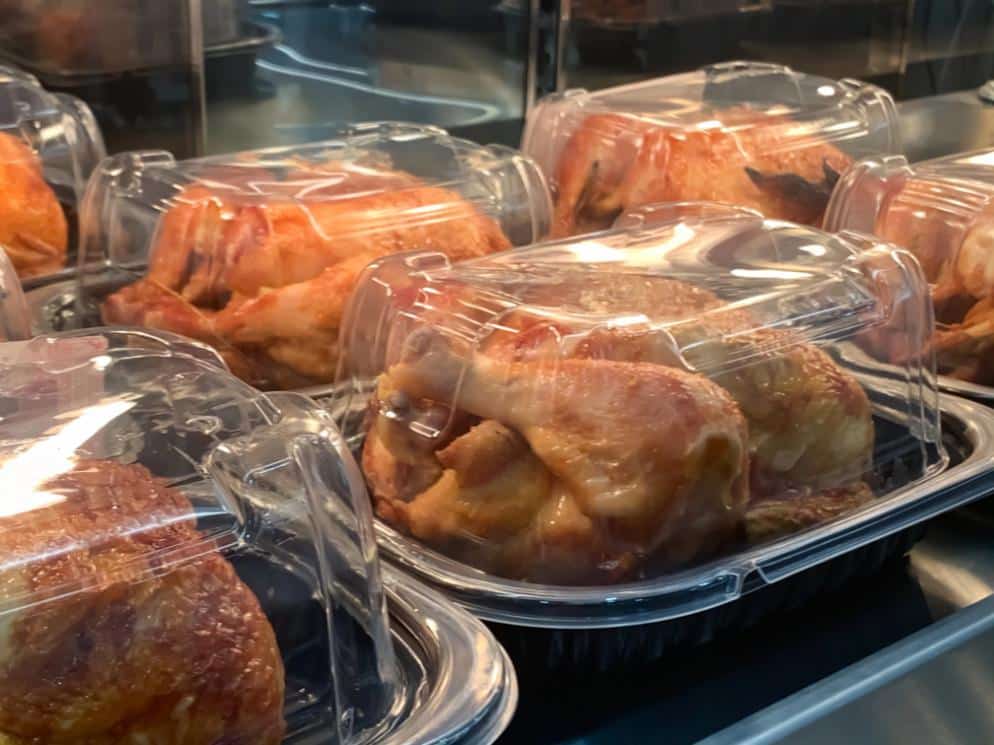 Plastic containers of rotisserie chickens in a cabinet at the grocery store