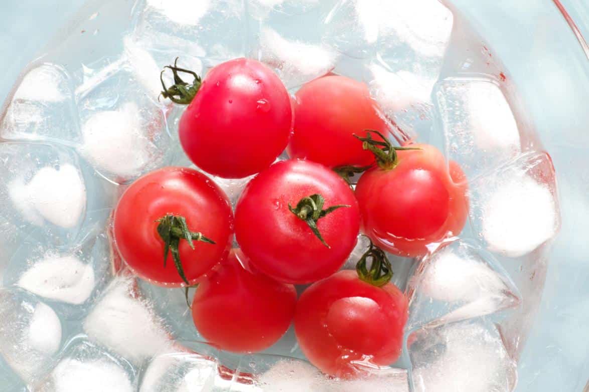 7 small tomatoes in a clear bowl with ice and water