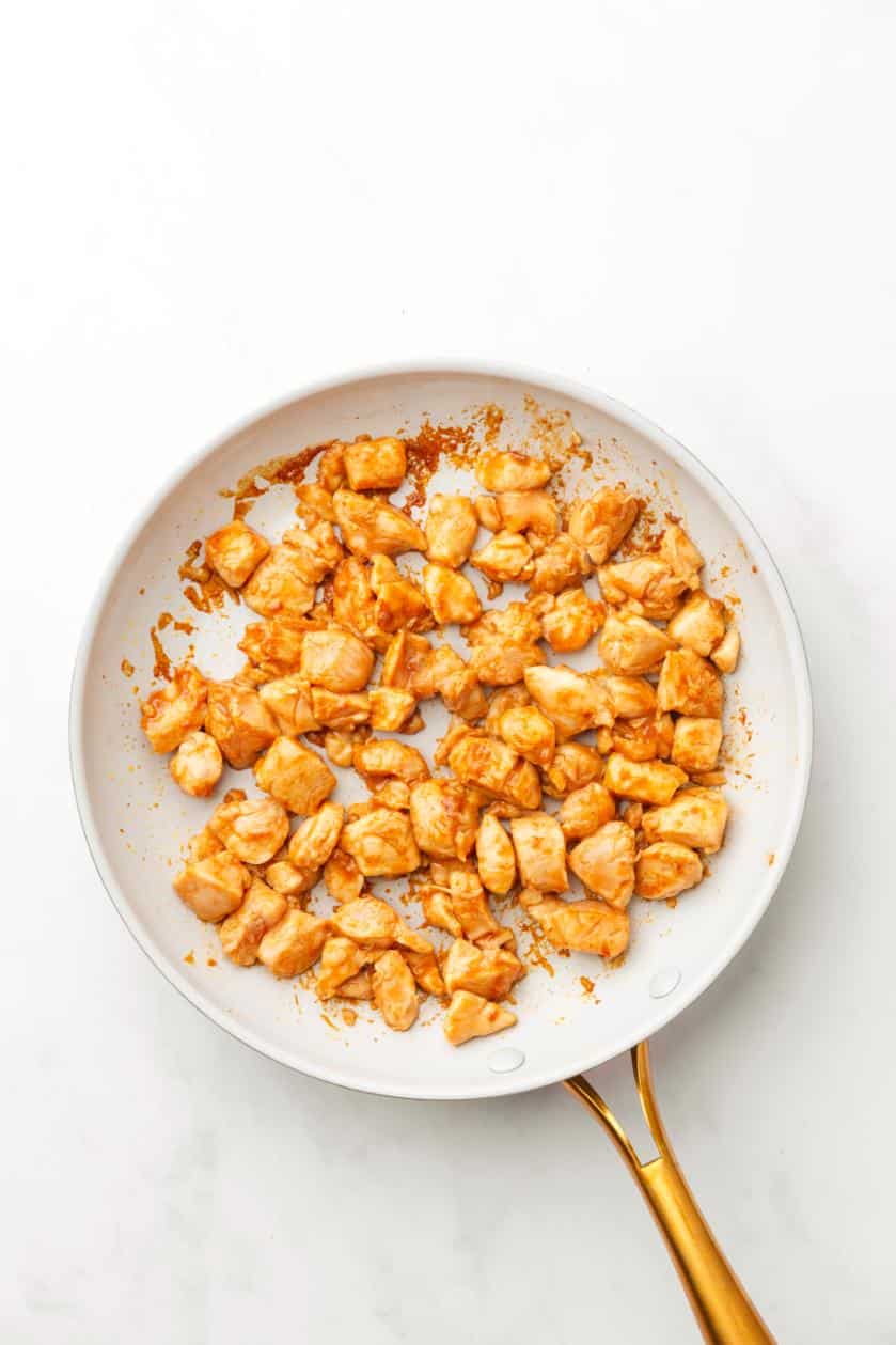A white saucepan with a gold handle contained stir-fried chicken pieces.
